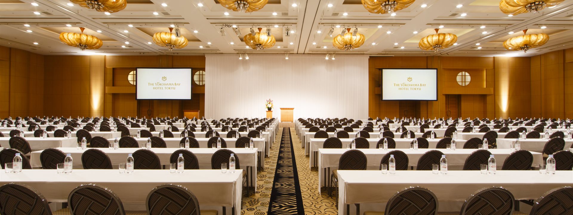 The scene in the "Queen's Grand Ballroom", the grand banquet hall of the Yokohama Bay Hotel Tokyu, shows a school-style layout with many long tables lined up. Photo taken from the rear, facing forward.