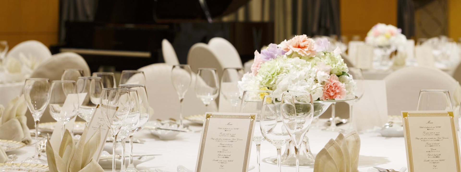 The banquet hall at the Yokohama Bay Hotel Tokyu is set for a formal dinner. A bouquet is placed in the center of the round table, and a grand piano is positioned at the back.